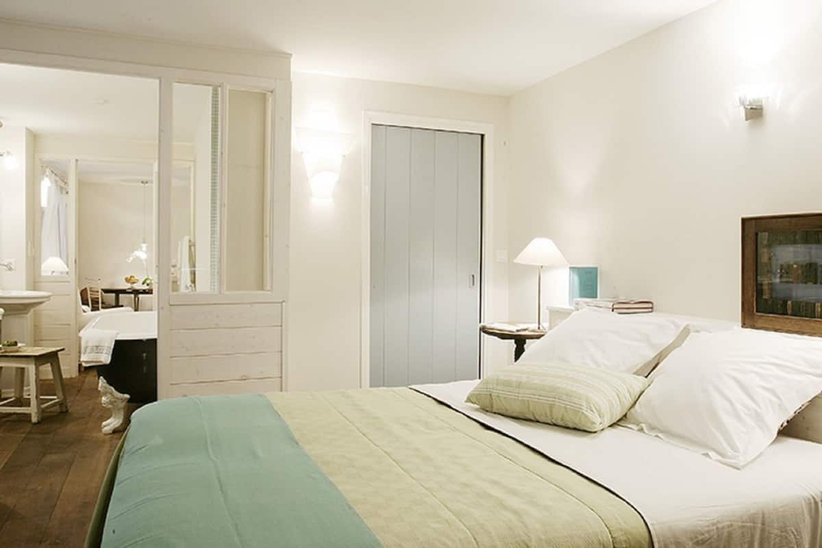 Quarto com cama, abajures, espelho, cômoda e janela com vista.