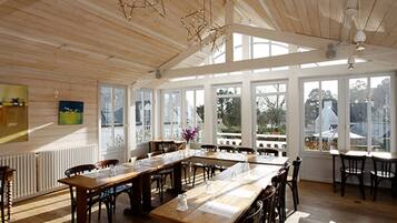 A spacious dining area with wooden tables and chairs, large windows, and a high ceiling with exposed beams.