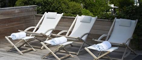 Ein Poolbereich mit Holzterrasse und weißen Liegestühlen mit Handtüchern.