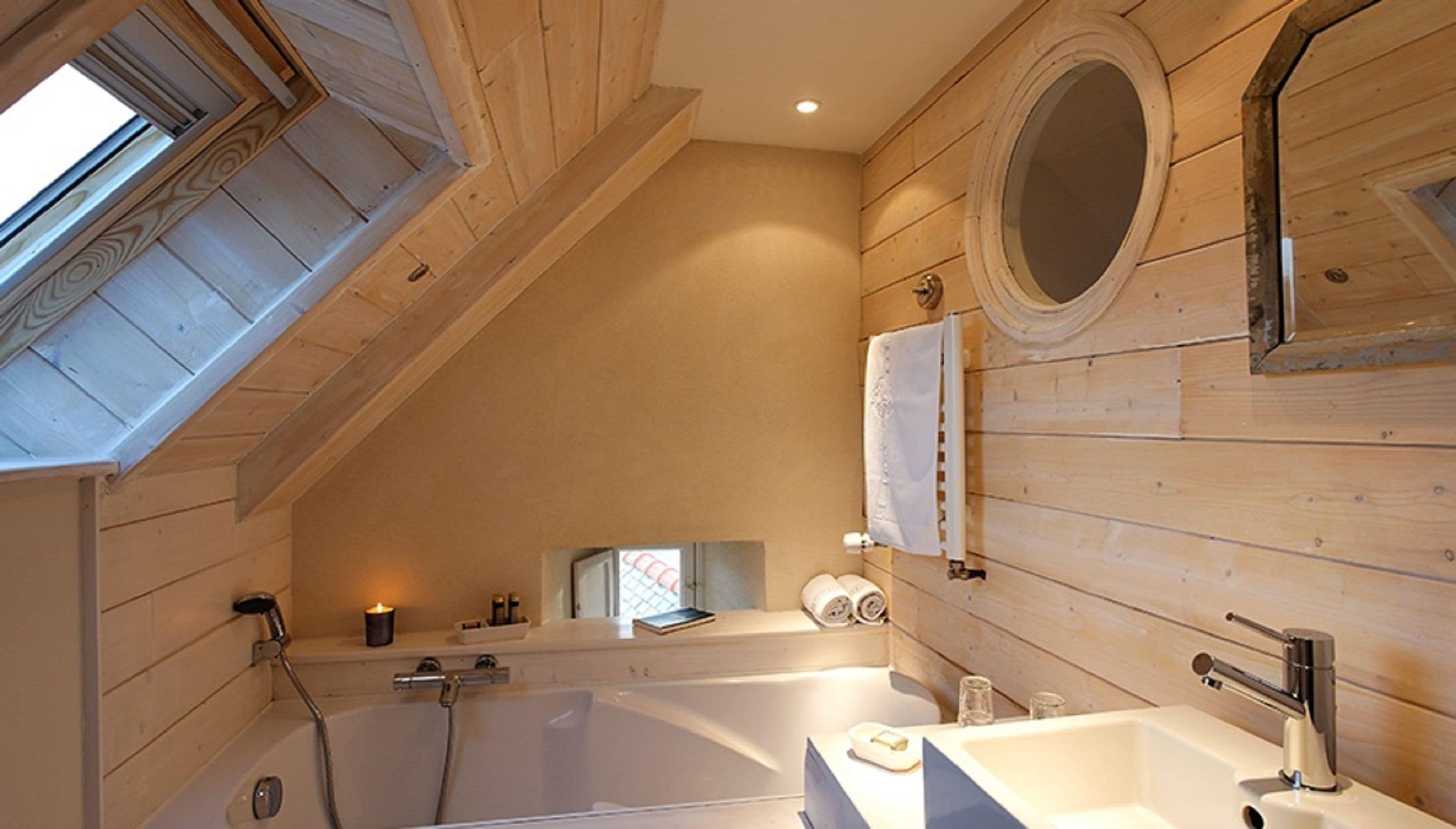 A wooden interior with a skylight, a bathtub, a sink, and a mirror.