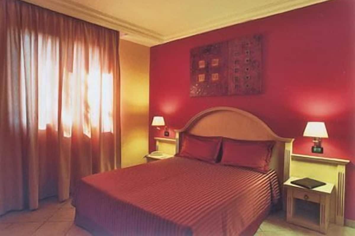 Una habitación de hotel con una cama grande, dos lámparas de noche y una pared roja.