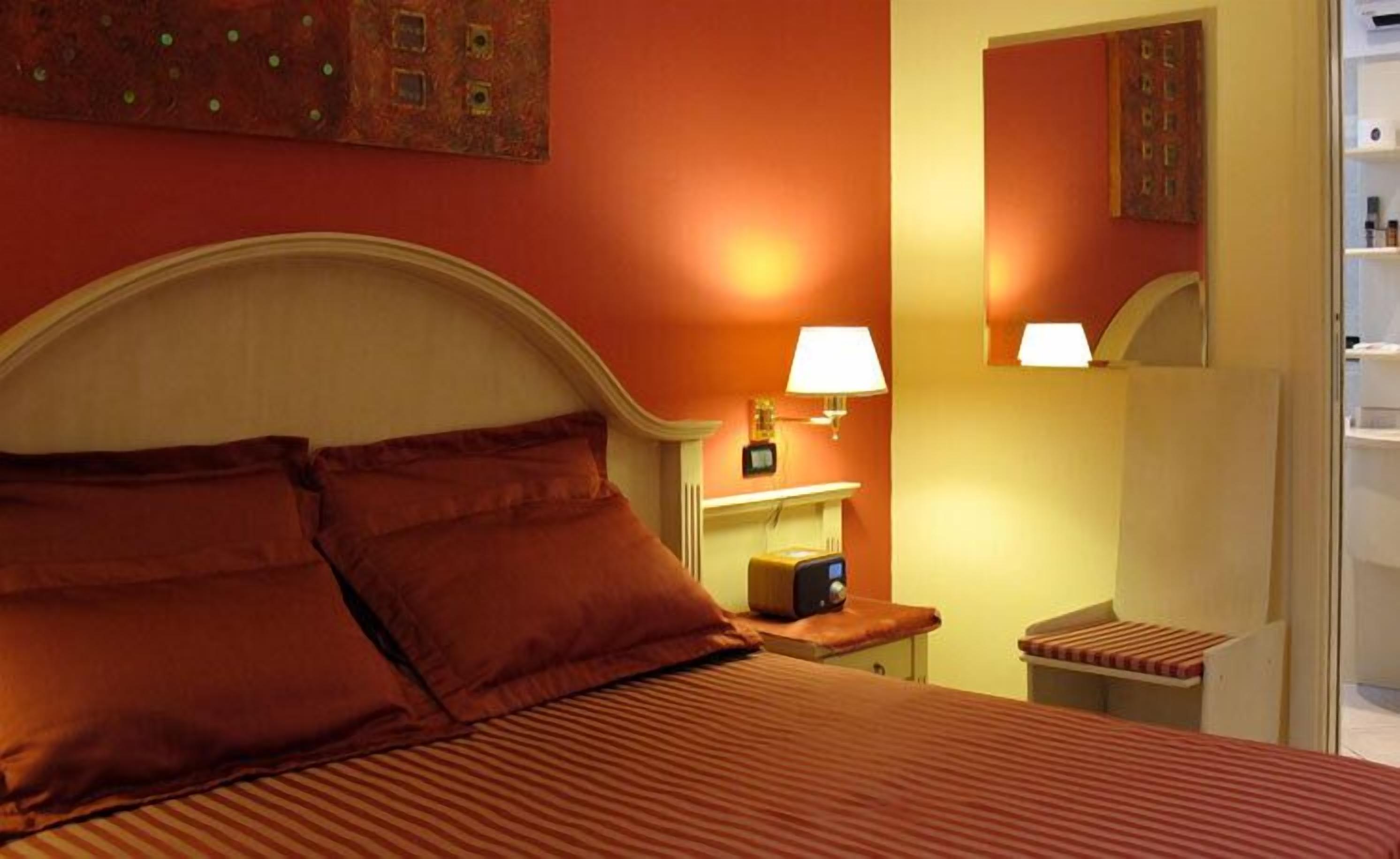 A hotel room with a large bed, a bedside table with a lamp, and a small nightstand.