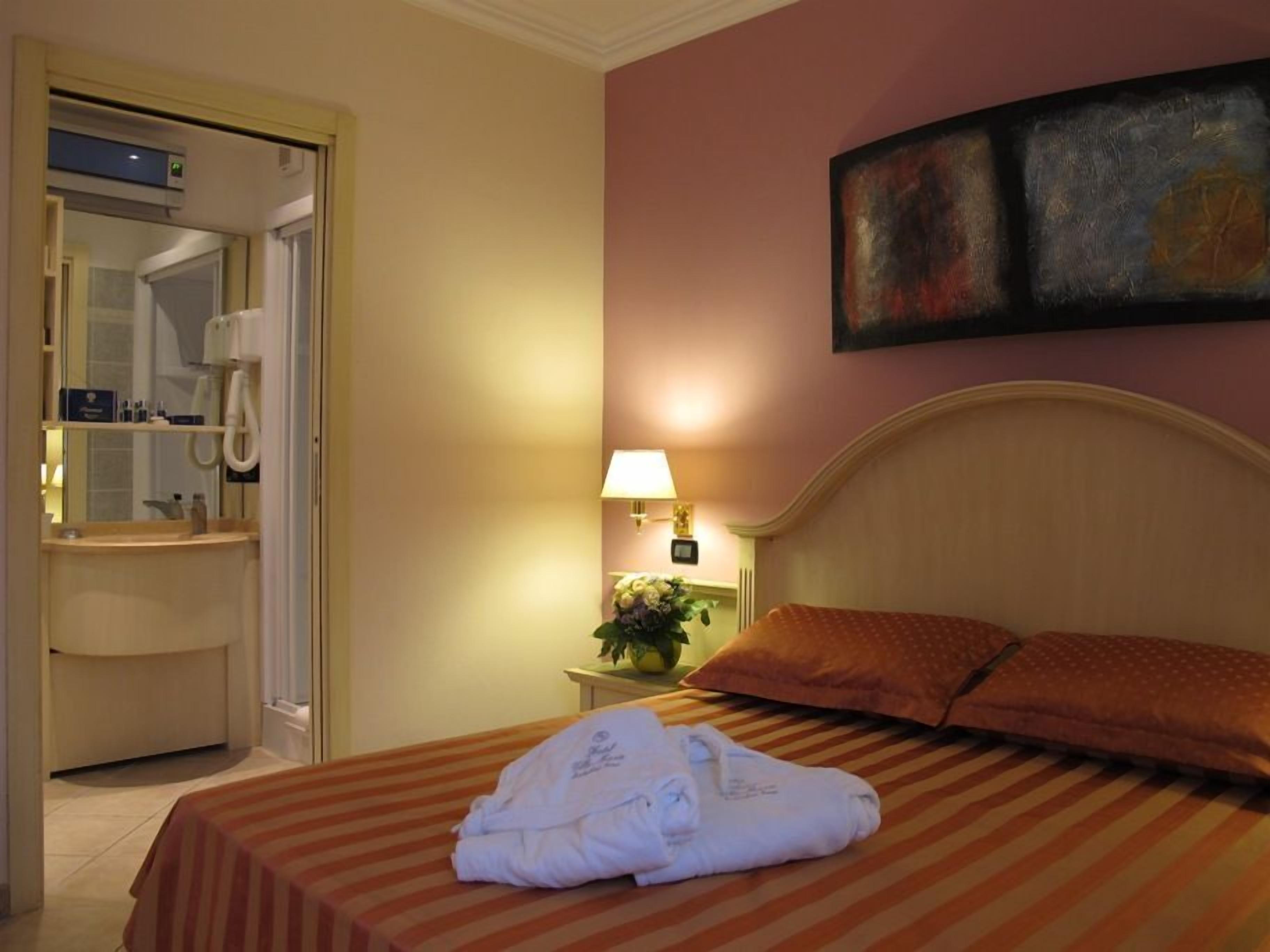 Quarto de hotel com cama, mesa de cabeceira com luminária, espelho e um quadro na parede.
