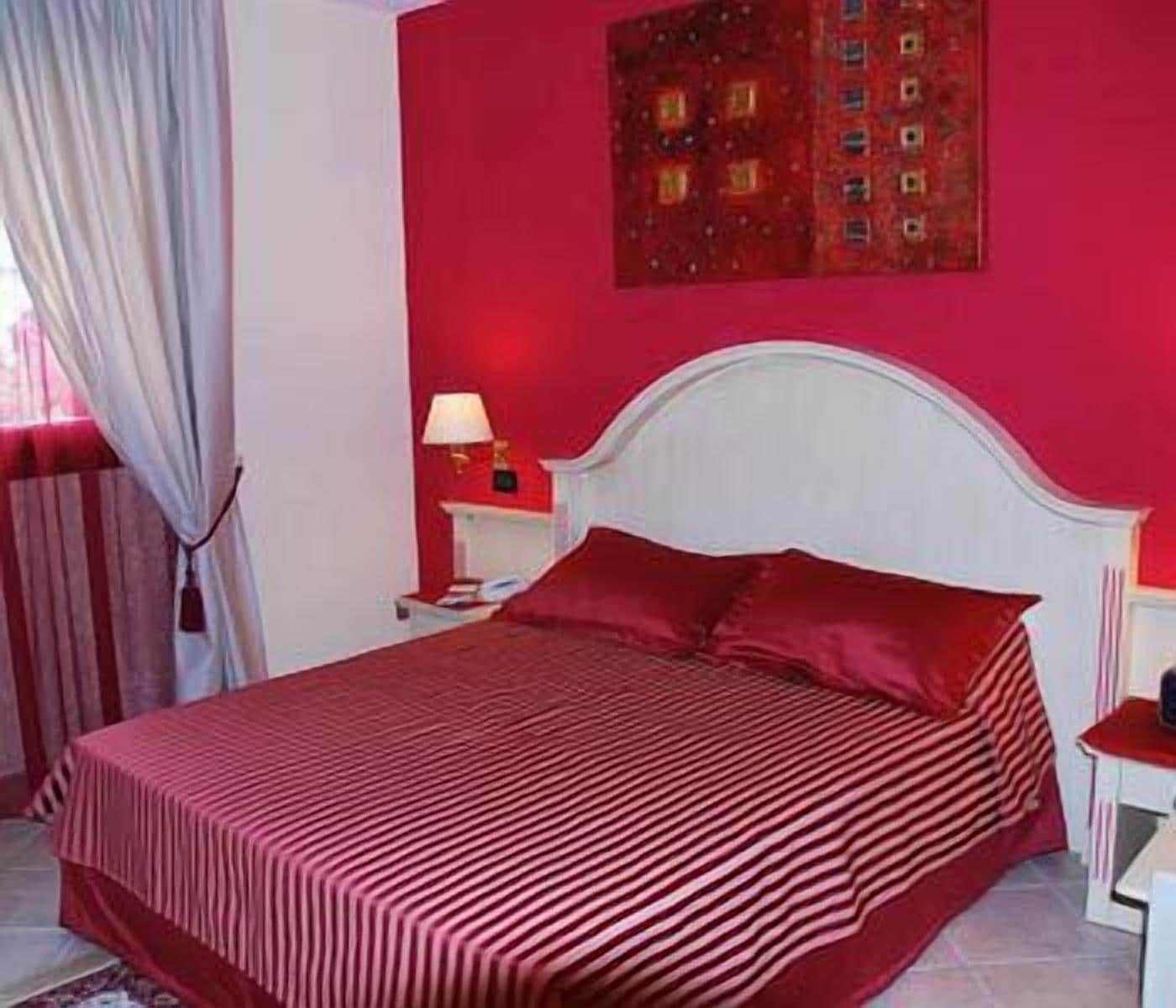 A room with a bed, a nightstand, a lamp, and a window with curtains.