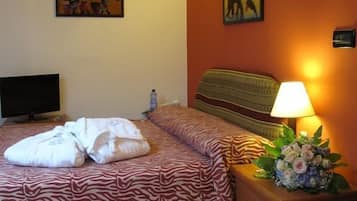 Een hotelkamer met een bed, een televisie, een nachtkastje met een lamp en bloemen, en twee schilderijen aan de muur.