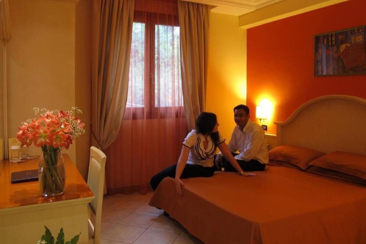 Una habitación de hotel con cama, un escritorio con un florero y una ventana con cortinas.