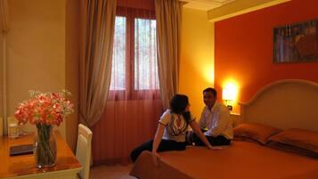 A hotel room with a bed, a desk with a vase of flowers, and a window with curtains.
