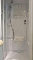 Una ducha a ras de suelo con mampara de vidrio, cabezal de ducha de mano y asiento integrado.