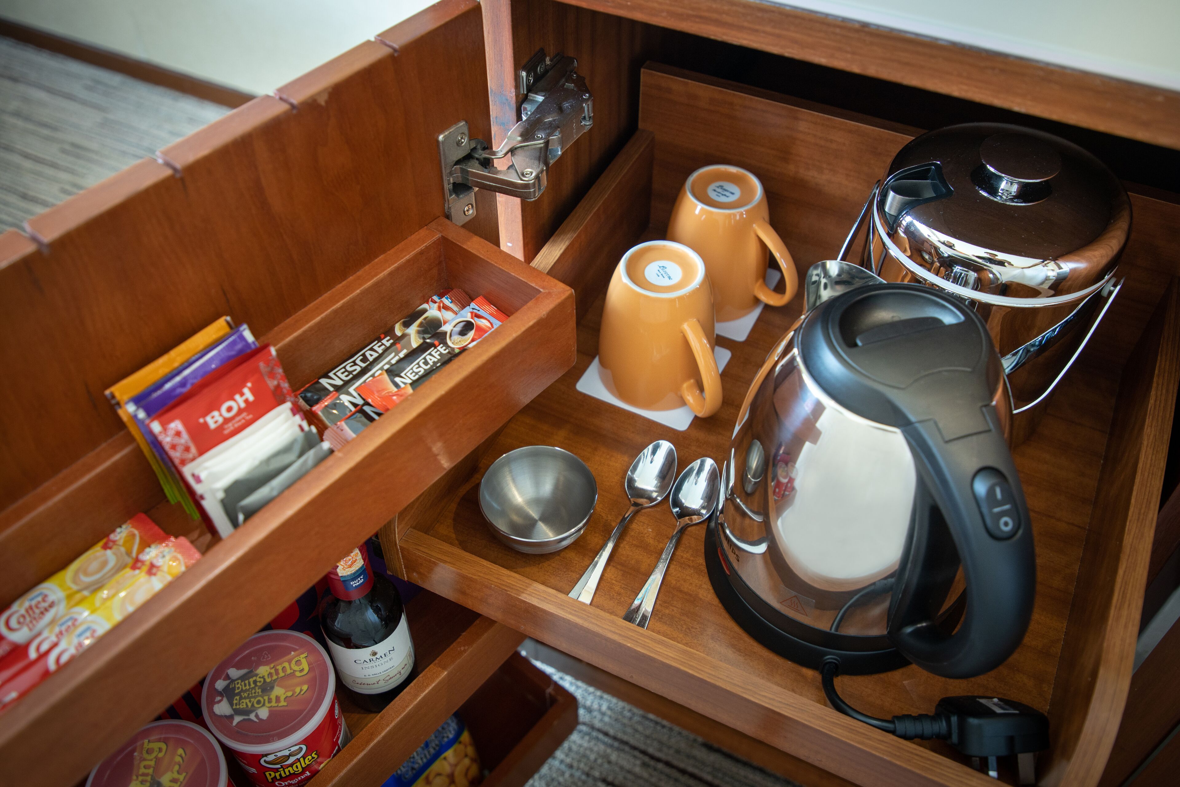 A wooden drawer with a coffee maker, two mugs, a bowl, and utensils.