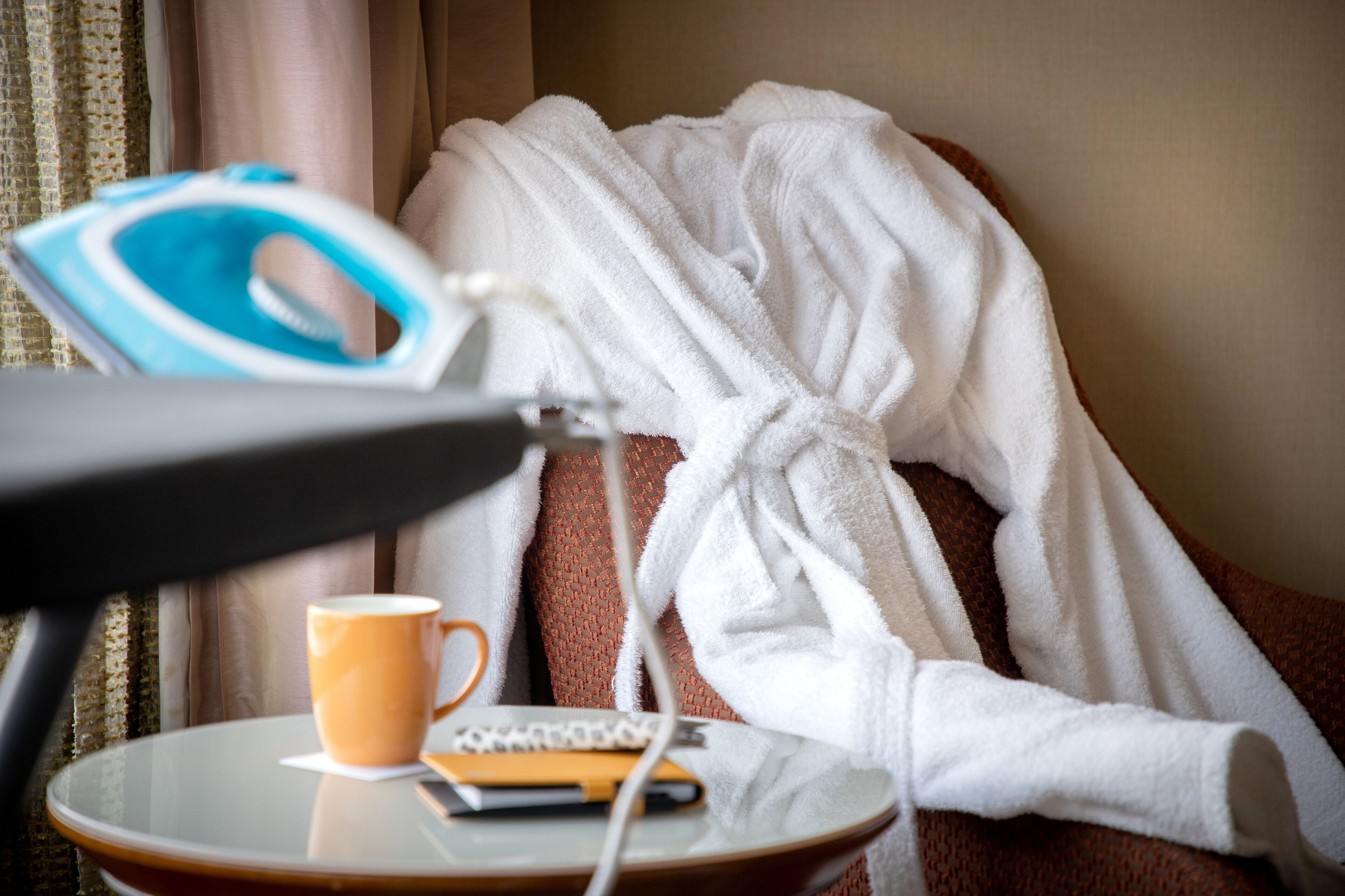 Habitación de hotel con una cama cubierta con un albornoz blanco, una mesa con una taza de café, una plancha y un control remoto.
