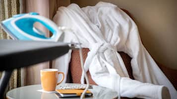 Habitación de hotel con una cama cubierta con un albornoz blanco, una mesa con una taza de café, una plancha y un control remoto.