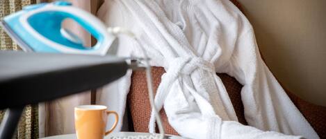 Habitación de hotel con una cama cubierta con un albornoz blanco, una mesa con una taza de café, una plancha y un control remoto.