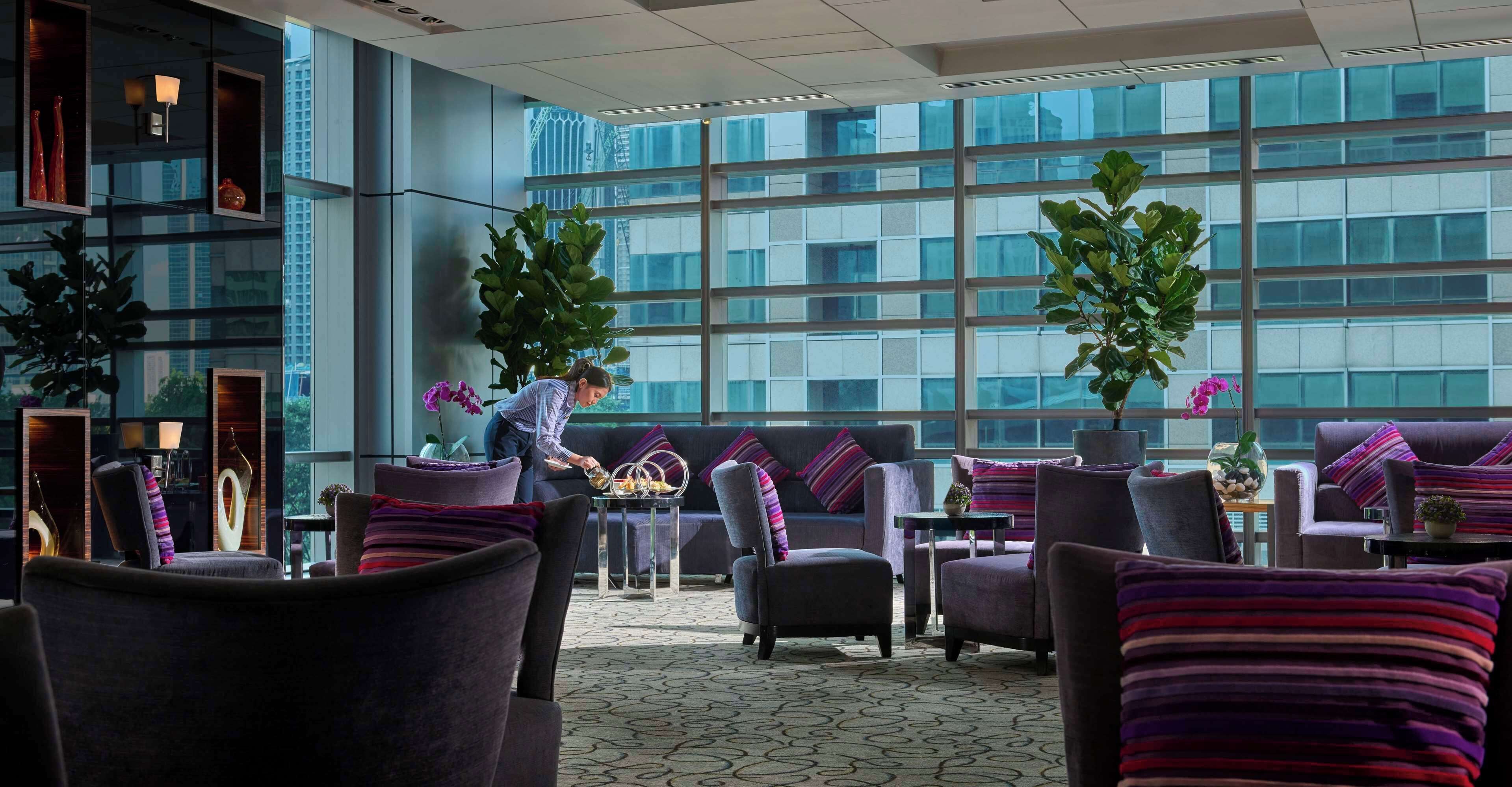 A modern lounge area with comfortable seating, large windows, and decorative plants.
