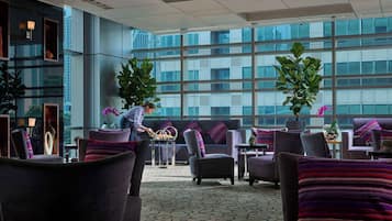 A modern lounge area with comfortable seating, large windows, and decorative plants.