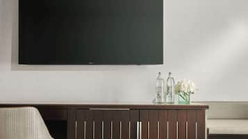 Een moderne woonkamer met een flatscreen televisie aan de muur, een houten kast met glazen flessen en bloemen, en een fauteuil met een patroon.