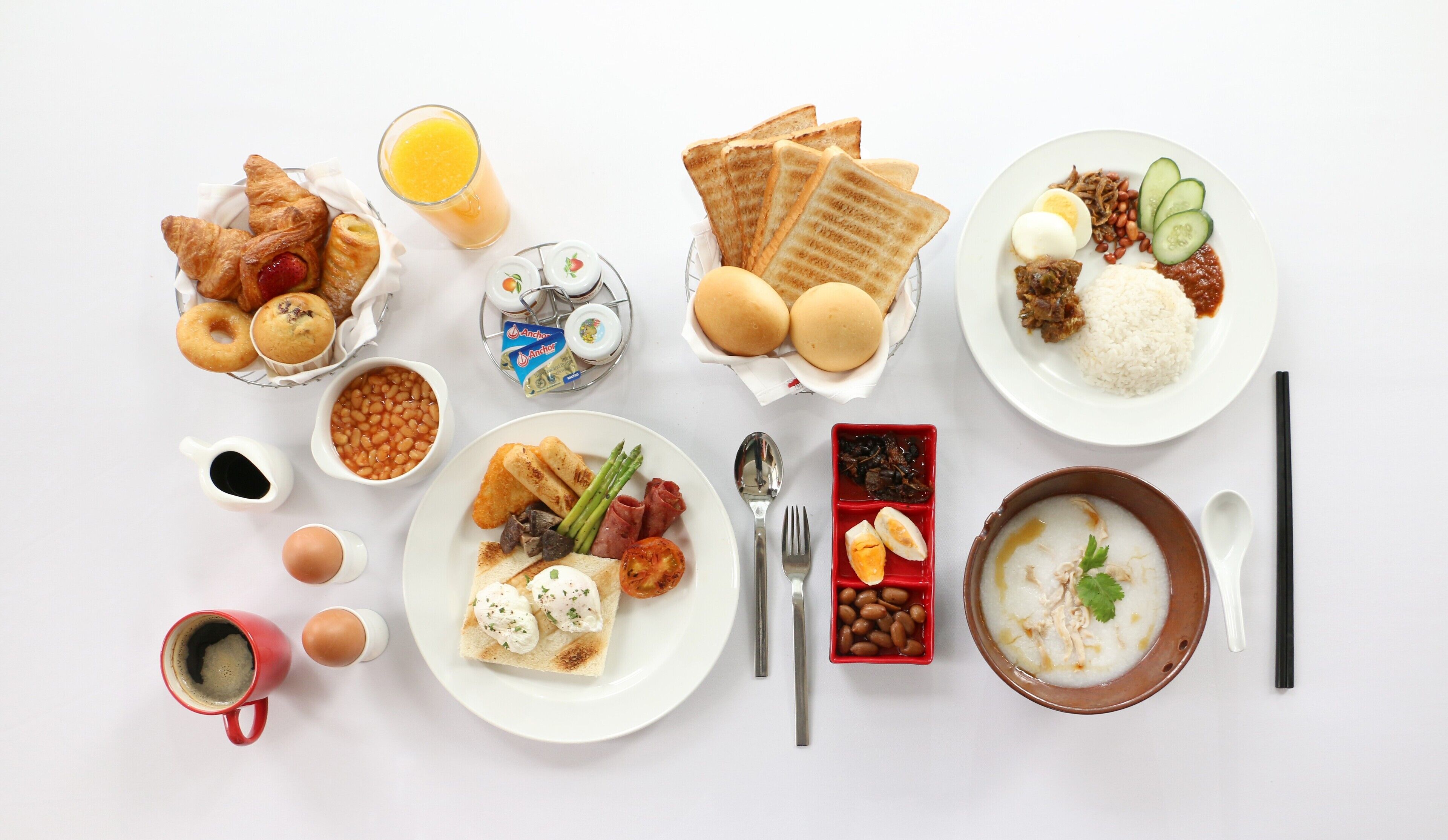 A breakfast spread with croissants, toast, eggs, beans, asparagus, and a bowl of soup.