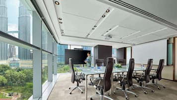 A modern conference room with a glass table, leather chairs, a large screen, and a city view.