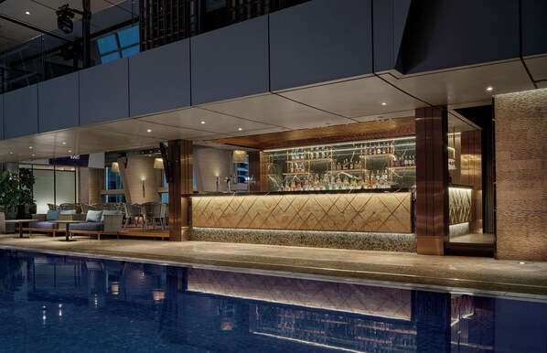 Zona de bar moderna con área de estar junto a la piscina, mostrador de bar y piscina.
