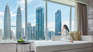 A modern living room with a large window offering a view of the Petronas Towers and other high-rise buildings. - Traders Hotel Kuala Lumpur (Kuala Lumpur)