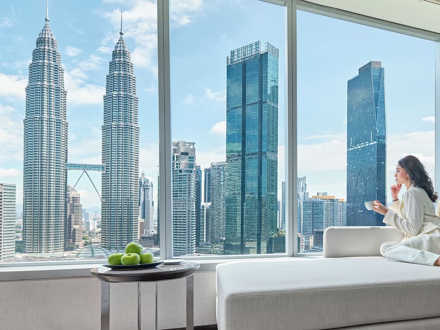 A modern living room with a large window offering a view of the Petronas Towers and other high-rise buildings.