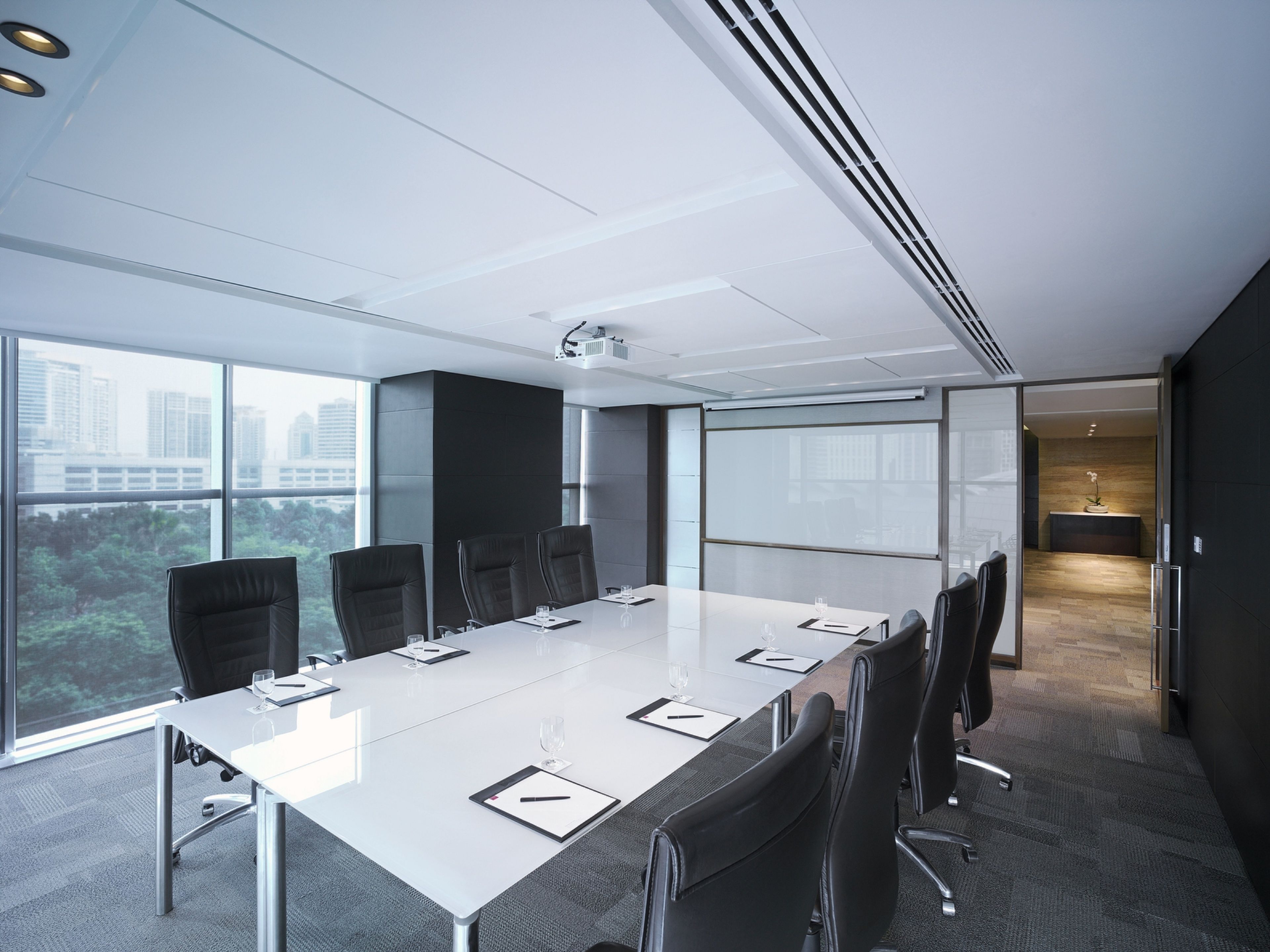 A modern conference room with a long table, black chairs, and a large window offering a city view.