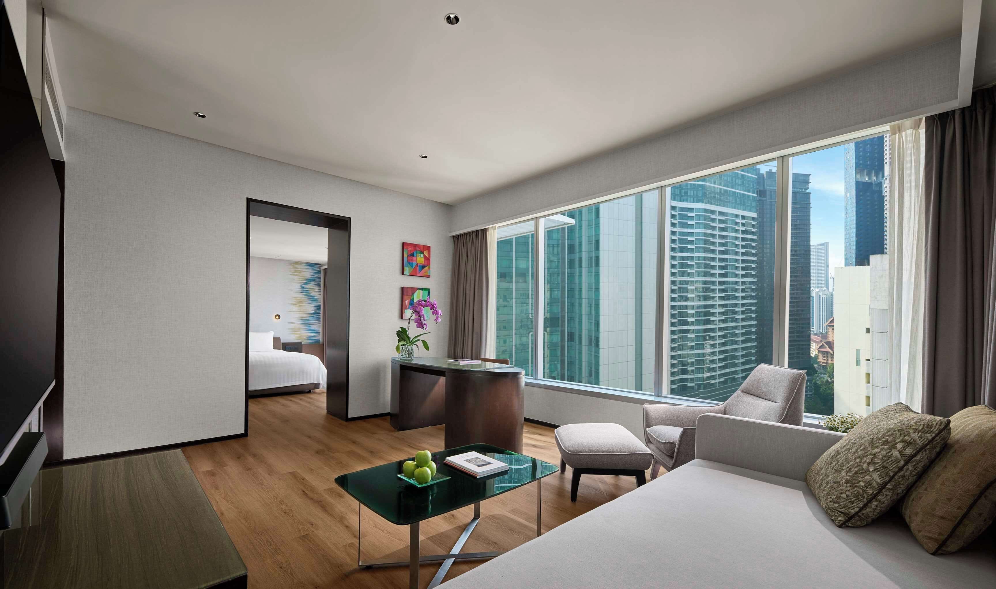 A modern hotel room with a large window, a bed, a desk, and a seating area.