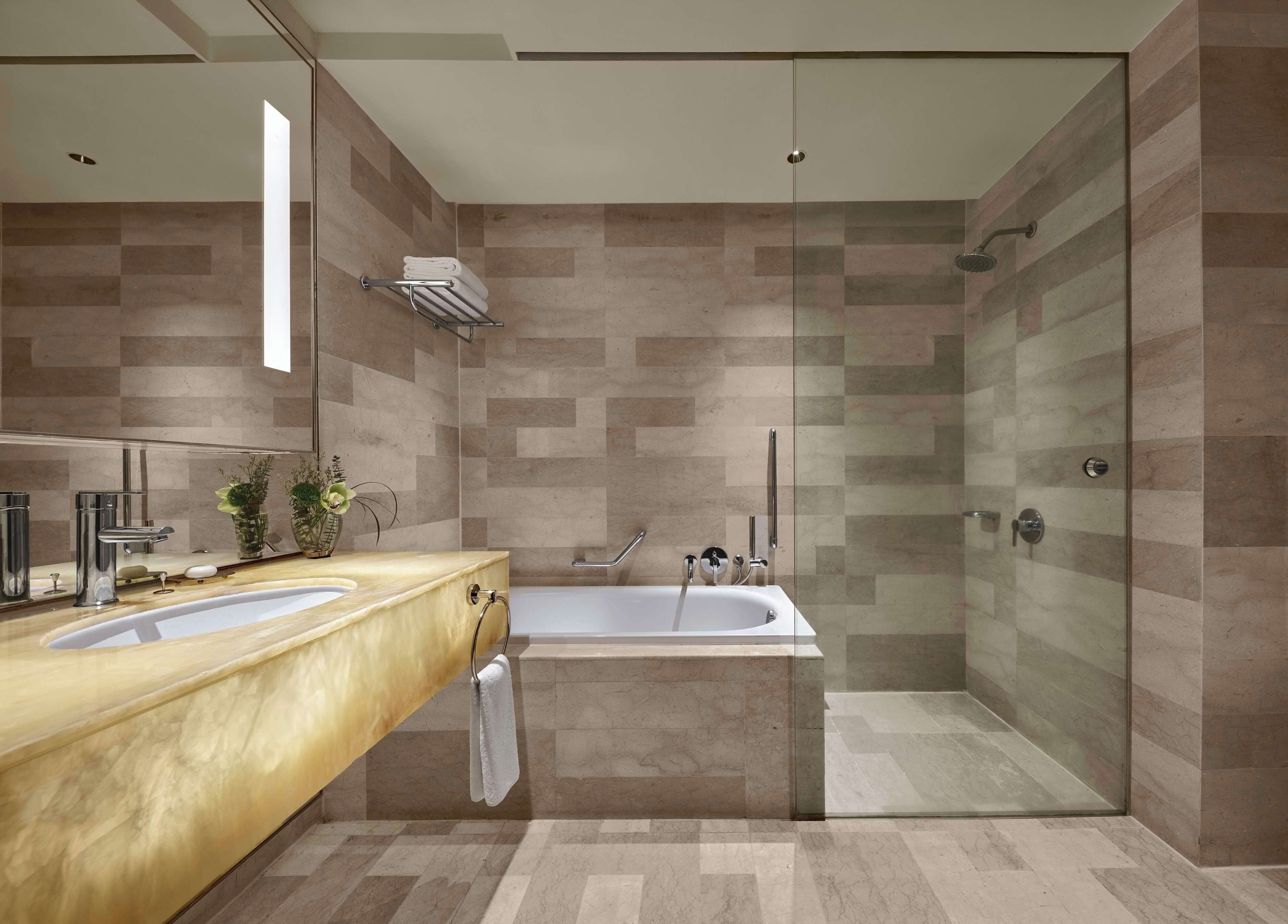 Un baño moderno con tocador de madera, dos lavabos, bañera y zona de ducha con mampara de cristal.