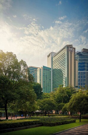 A modern urban park with tall buildings in the background, including a hotel with a prominent sign.