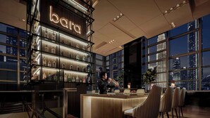Un bar avec une enseigne au néon, des étagères remplies de bouteilles d’alcool et une vue sur la ville à travers de grandes fenêtres.