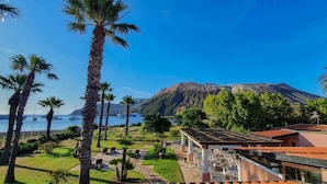 Un hotel frente al mar con terraza al aire libre, palmeras y vistas a la montaña y al océano.