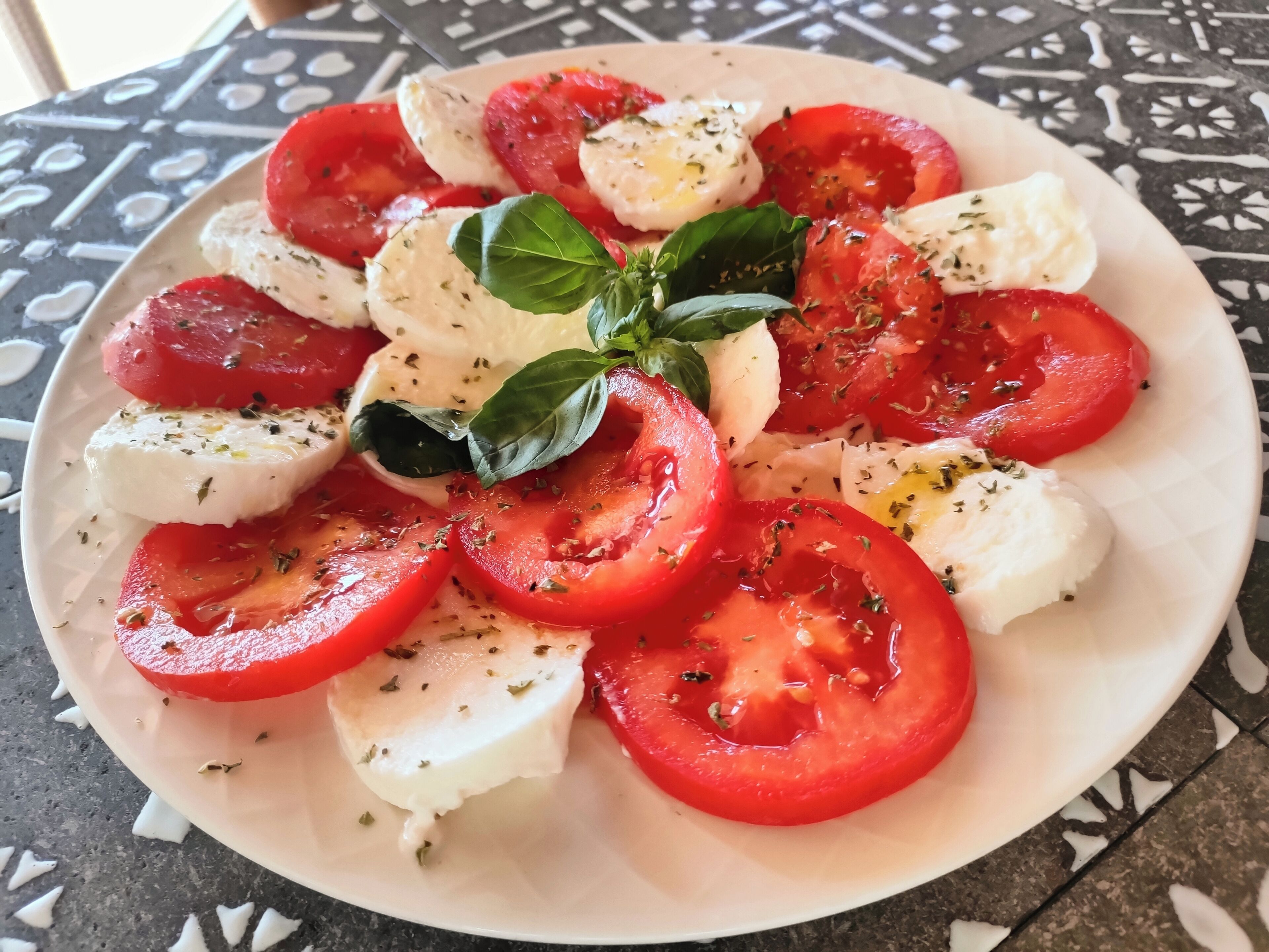Une assiette de salade caprese, composée de tomates, de mozzarella et de basilic.