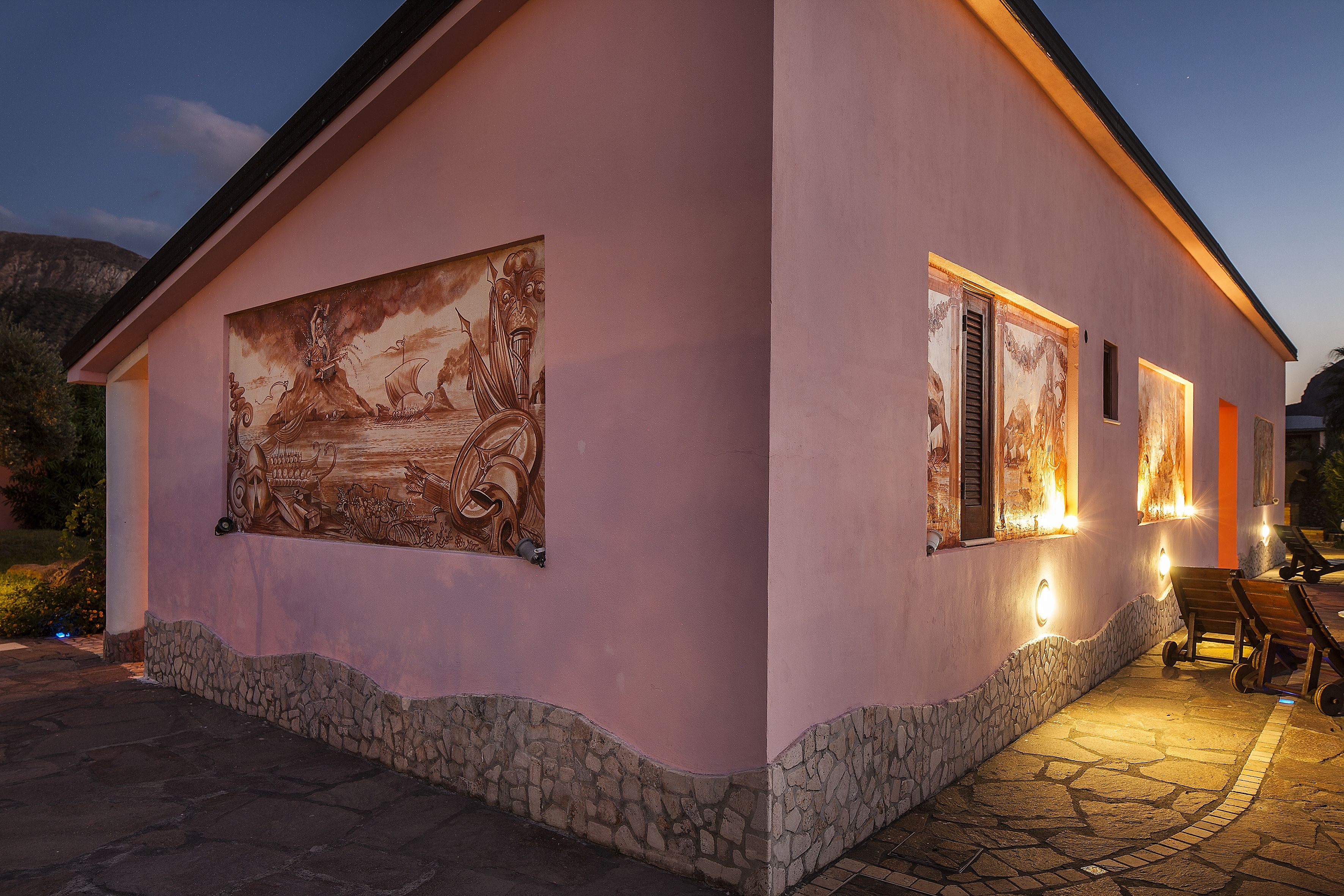 A pink building with a mural, stone steps, and outdoor seating.