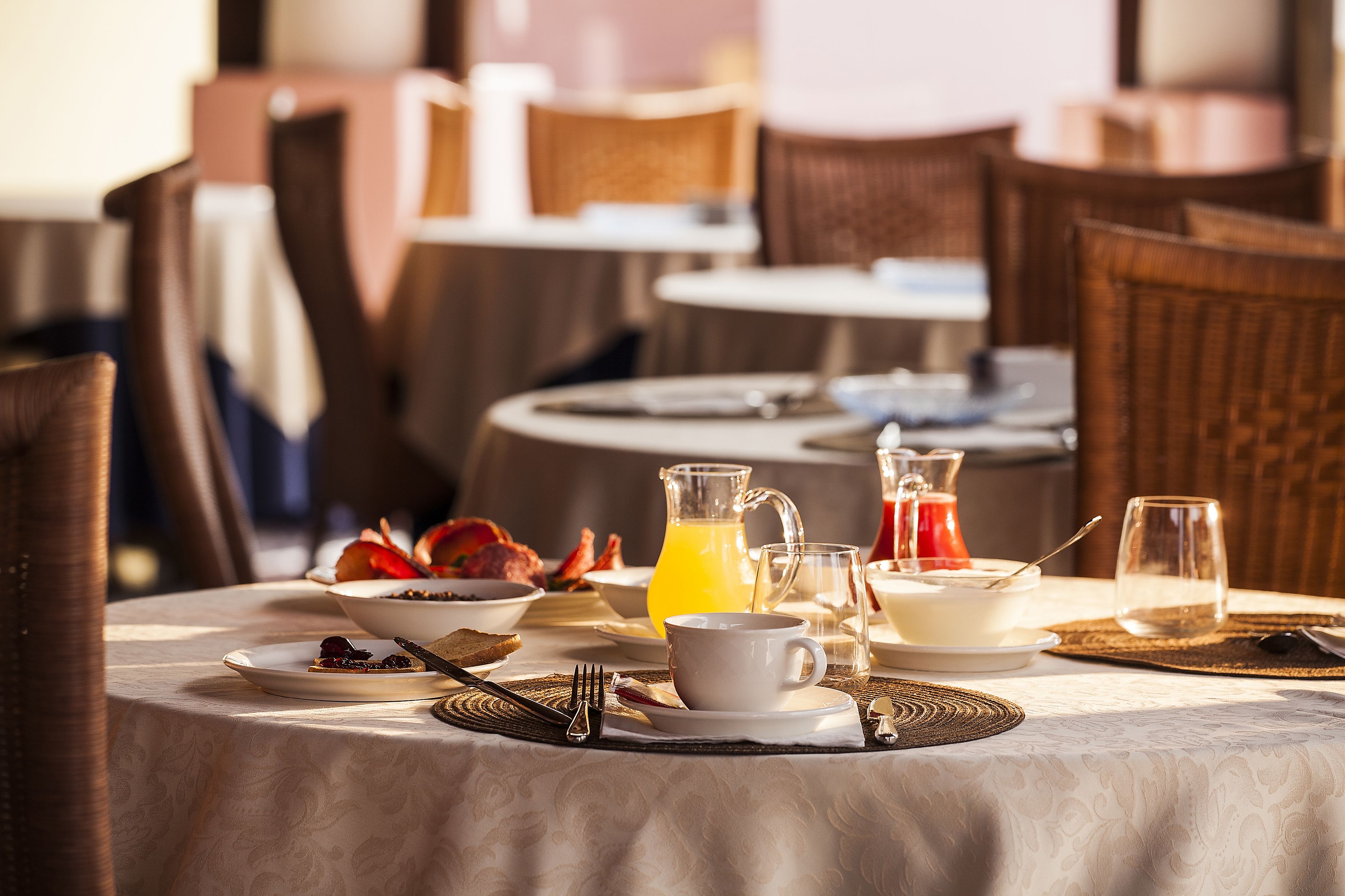 Una mesa de desayuno dispuesta con platos, tazones, una jarra de jugo de naranja y una taza.