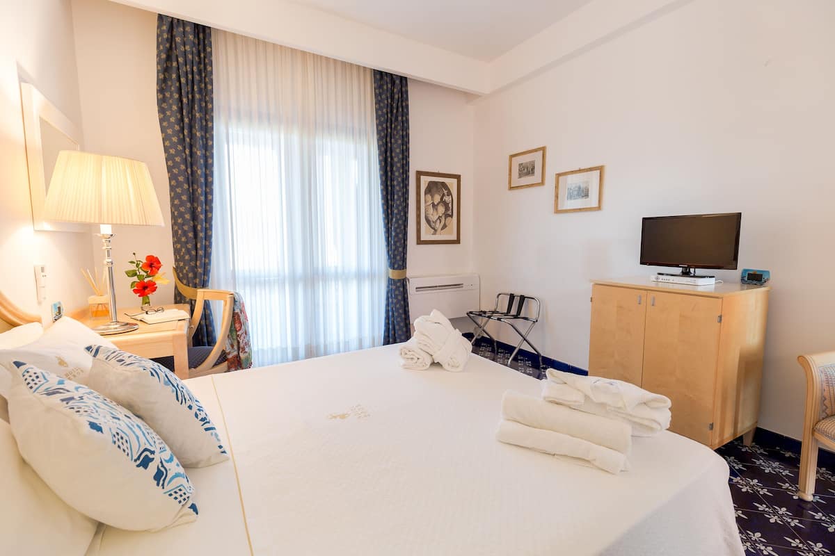 A hotel room with a bed, a desk with a lamp, a chair, a TV, and a wardrobe.