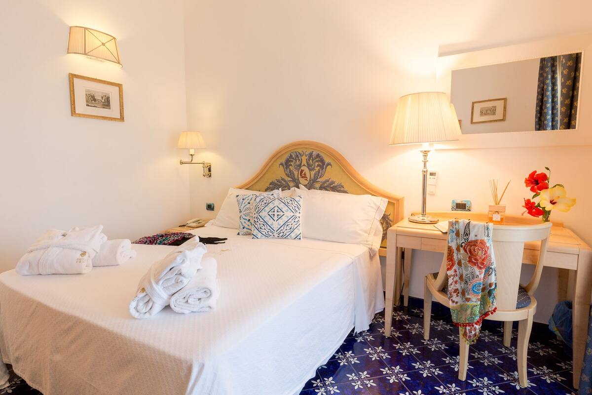 A hotel room with a bed, bedside lamps, a desk with a chair, and a mirror.