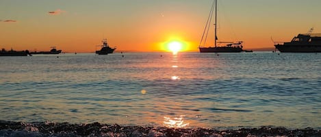 A sunset over a calm sea with boats and a pier.