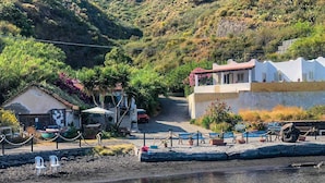 Una zona costera con un edificio pequeño, un muelle con barcos y una colina al fondo.
