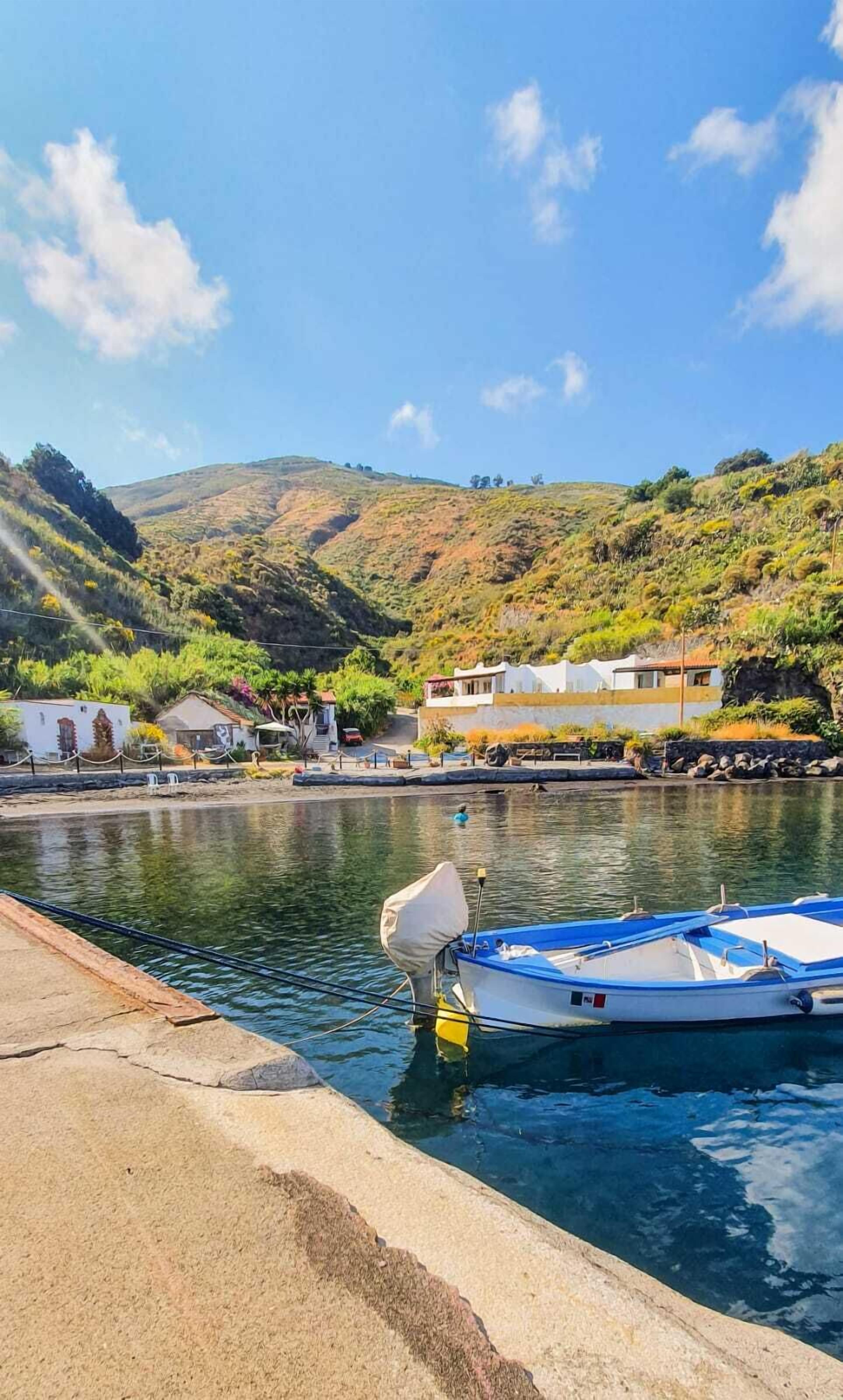 A marina with boats docked, a calm water body, and a hilly landscape in the background.