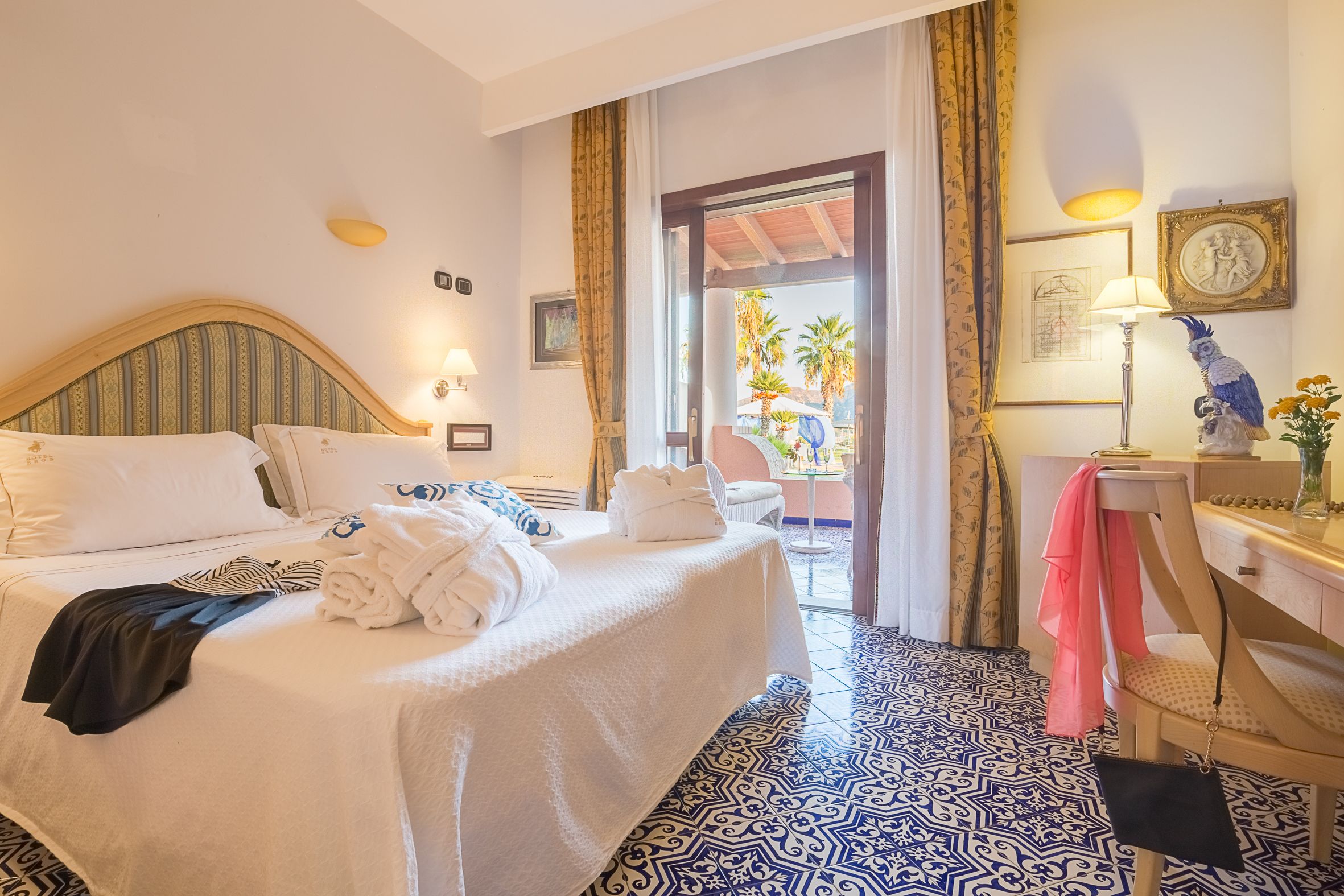 A hotel room with a bed, a desk, a chair, and a view of palm trees outside.