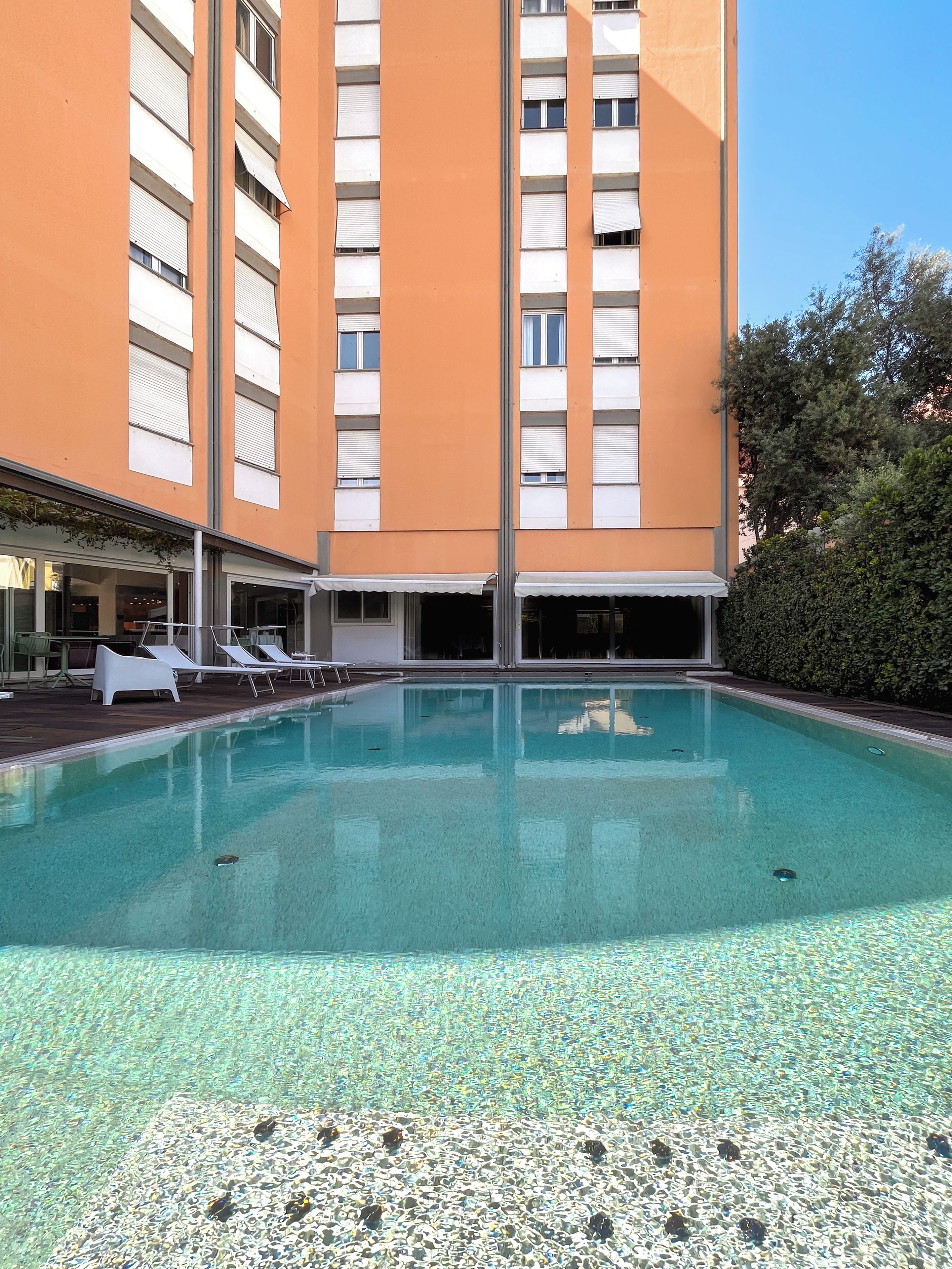 A swimming pool with clear water, surrounded by lounge chairs and a building with multiple windows.