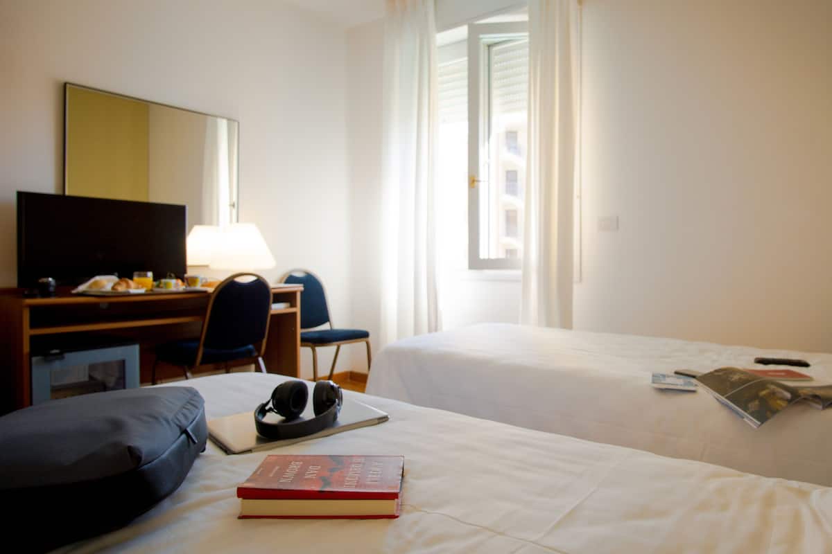 A hotel room with two beds, a desk with a chair, a television, and a window with curtains.