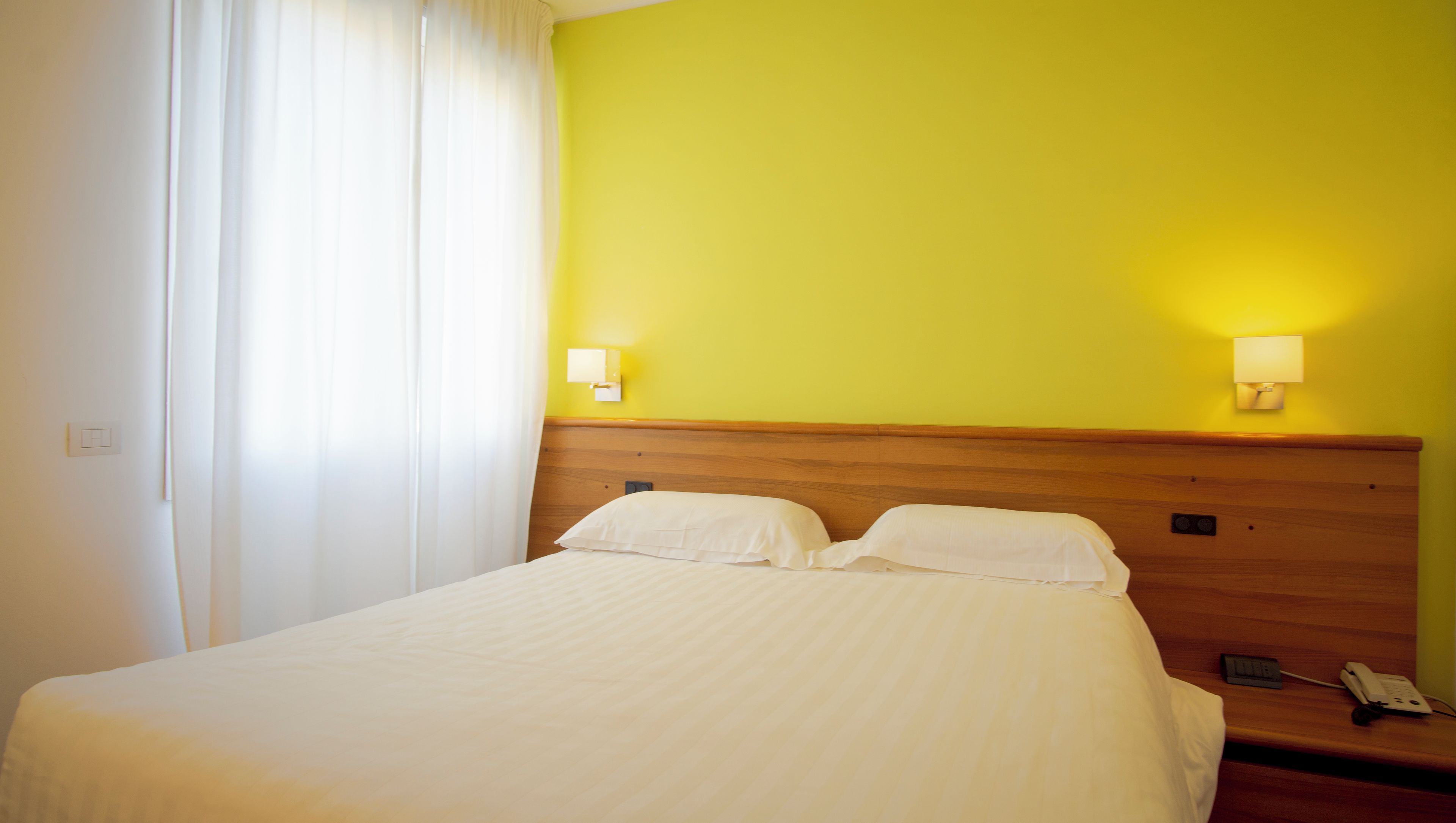 A hotel room with a bed, two bedside lamps, a nightstand, and a telephone.