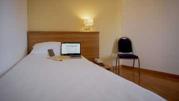 Habitación de hotel con cama, una laptop sobre la cama, una silla y una mesita de noche con un teléfono.