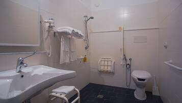 Ein Badezimmer mit Waschbecken, Toilette, Dusche und Haltegriffen.