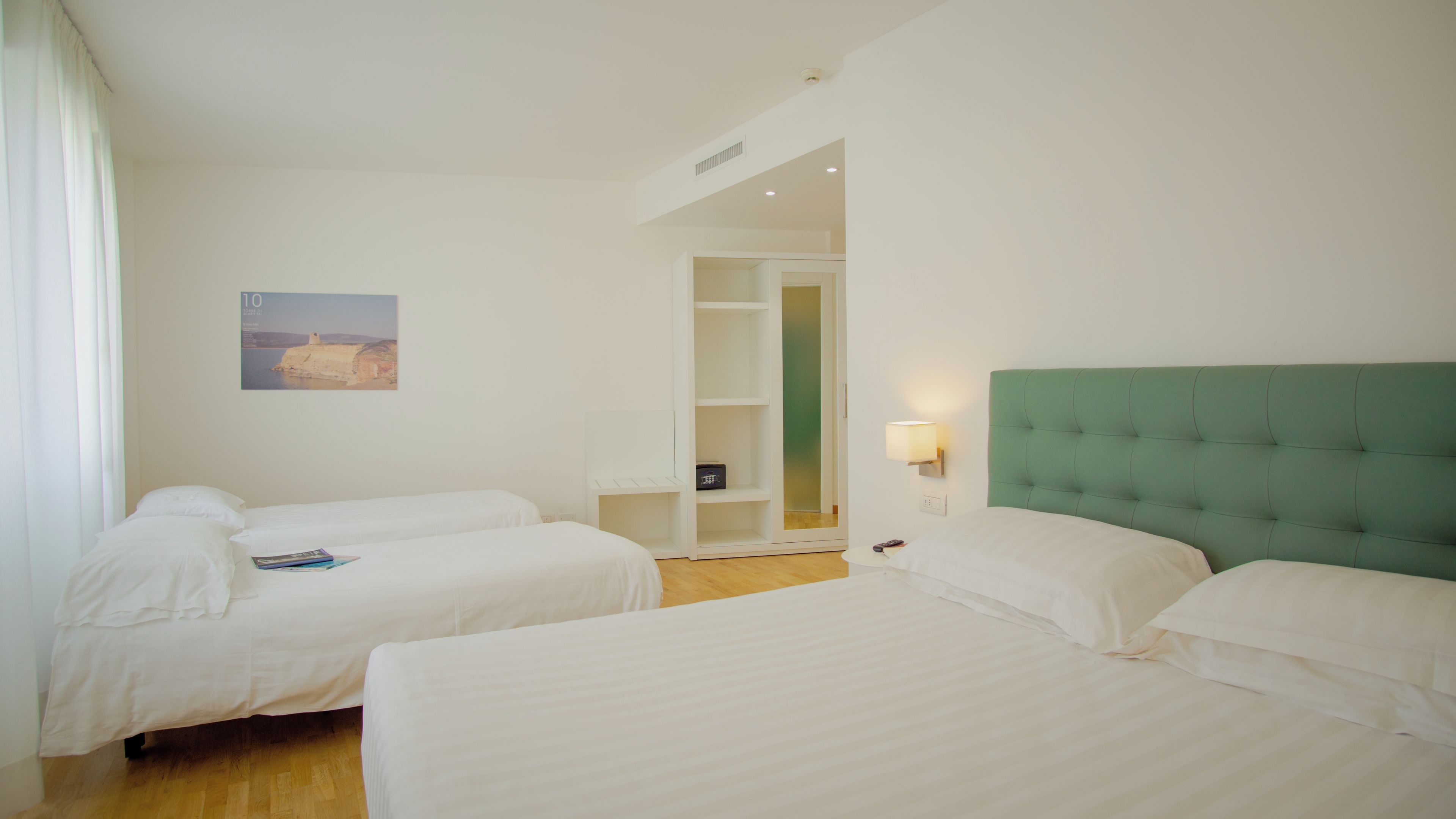 A hotel room with two beds, a wardrobe, a bedside lamp, and a painting on the wall.