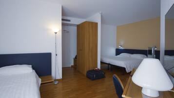 A hotel room with two beds, a desk, a chair, a lamp, and a wardrobe.