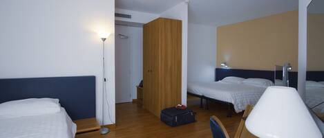 A hotel room with two beds, a desk, a chair, a lamp, and a wardrobe.