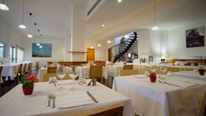 A restaurant with multiple tables set for dining, featuring white tablecloths, wine glasses, and cutlery. - Hotel Mistral 2 (Oristano)