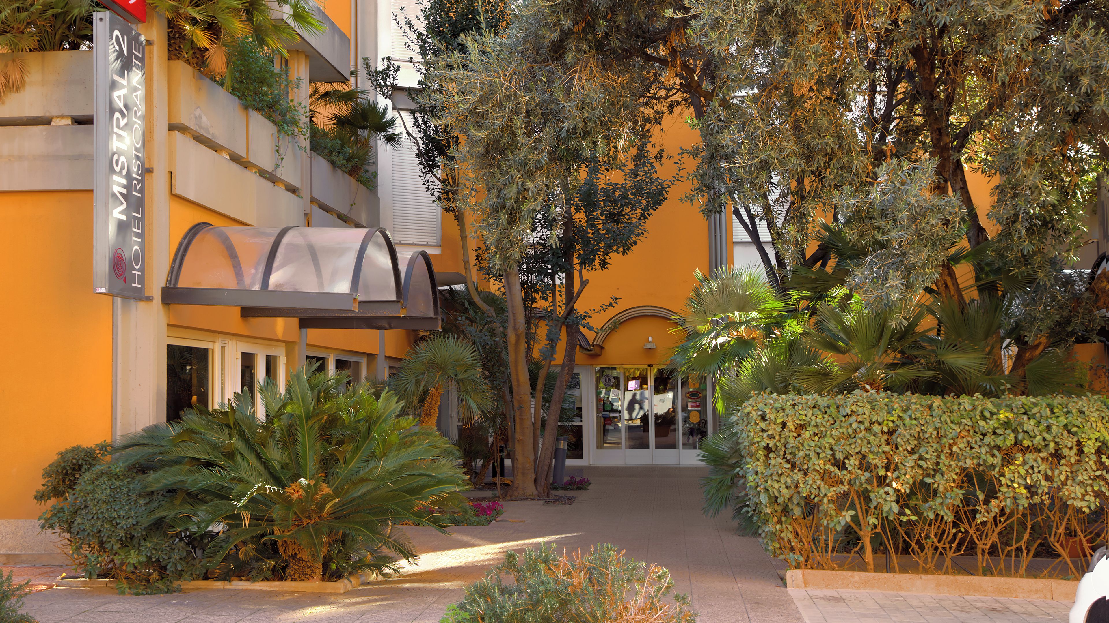 A hotel entrance with a covered walkway, surrounded by lush greenery and palm trees.