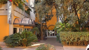 A hotel entrance with a covered walkway, surrounded by lush greenery and palm trees. - Hotel Mistral 2 (Oristano)